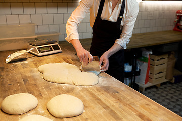 Image showing baker portioning dough with bench cutter at bakery