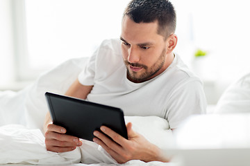 Image showing young man with tablet pc in bed at home bedroom