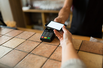 Image showing hands with payment terminal and smartphone at bar