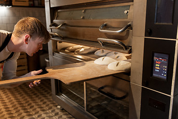 Image showing baker putting dough into bread oven at bakery