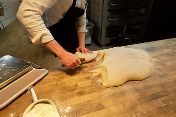 Image showing baker portioning dough with bench cutter at bakery