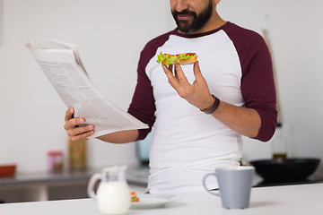 Image showing man reading newspaper and eating at home kitchen