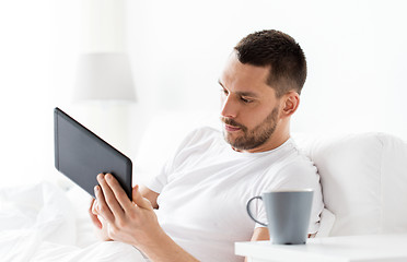 Image showing young man with tablet pc in bed at home bedroom