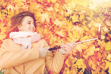 Image showing woman on autumn leaves taking selfie by smartphone