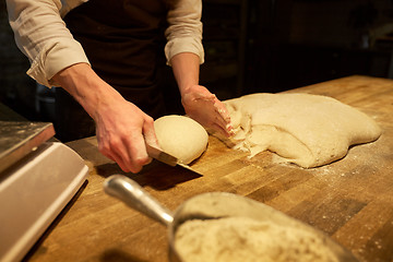 Image showing baker portioning dough with bench cutter at bakery