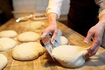 Image showing baker portioning dough with bench cutter at bakery