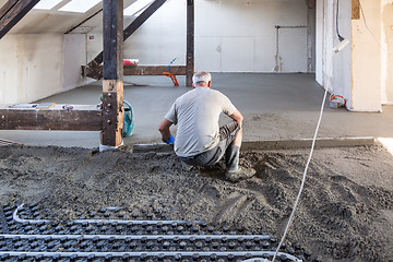 Image showing Laborer leveling sand and cement screed over floor heating.