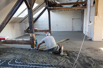 Image showing Laborer leveling sand and cement screed over floor heating.