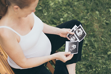 Image showing pregnant woman sitting on the bench and loocking ultrasound scan