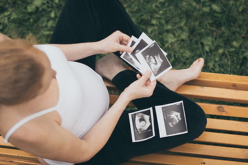 Image showing pregnant woman sitting on the bench and loocking ultrasound scan