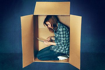 Image showing Introvert concept. Woman sitting inside box and working with laptop