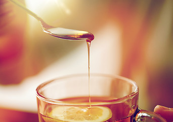 Image showing close up of woman adding honey to tea with lemon