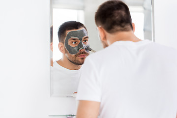 Image showing young man applying clay mask to face at bathroom