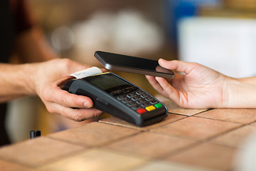 Image showing hands with payment terminal and smartphone at bar