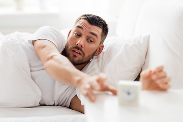 Image showing young man in bed reaching for alarm clock
