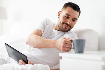 Image showing man with tablet pc drinking coffee in bed at home