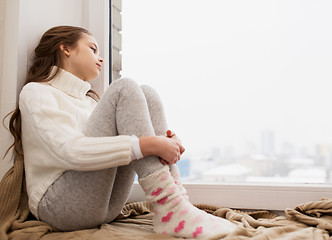 Image showing sad girl sitting on sill at home window in winter