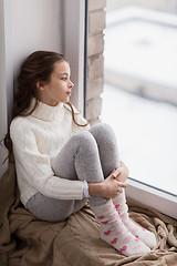 Image showing sad girl sitting on sill at home window in winter