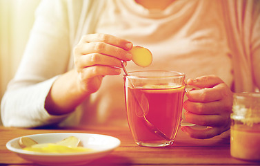 Image showing close up of woman adding ginger to tea with lemon