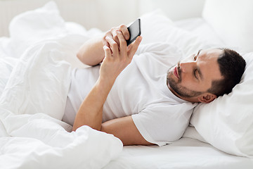 Image showing young man with smartphone in bed in morning