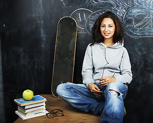 Image showing young cute teenage girl in classroom at blackboard seating on ta