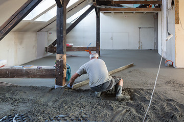 Image showing Laborer leveling sand and cement screed over floor heating.