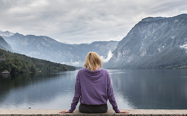 Image showing Woman wearing purple hoodie watching tranquil overcast morning scene at lake Bohinj, Alps mountains, Slovenia.