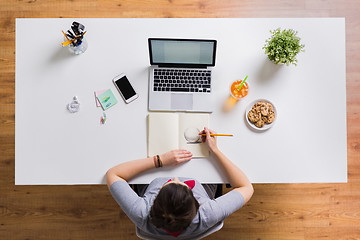 Image showing woman with laptop drawing in notebook at office