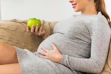 Image showing happy pregnant woman eating green apple at home