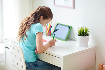 Image showing girl with tablet pc writing to notebook at home