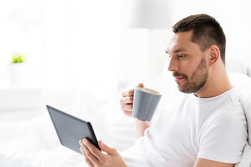 Image showing man with tablet pc drinking coffee in bed at home