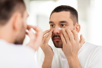 Image showing young man applying cream to face at bathroom