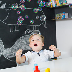 Image showing Portrait of cute toddler boy amazed by milky bubbles.