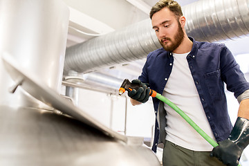 Image showing man with hose working at craft beer brewery kettle