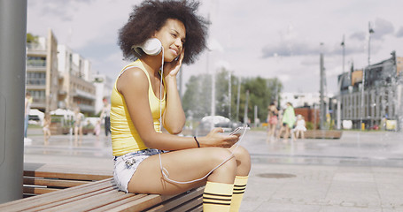 Image showing Model in headphones sitting on bench