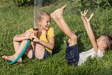 Image showing Happy kids sitting on the grass and pouring water from a hose.