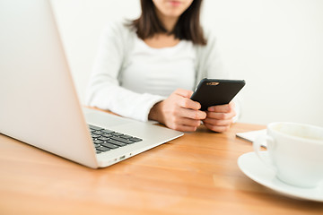 Image showing Woman sending sms on cellphone with her laptop computer