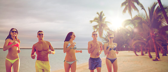 Image showing smiling friends in sunglasses running on beach