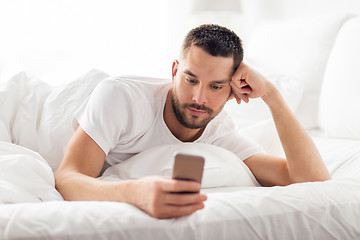 Image showing young man with smartphone in bed in morning