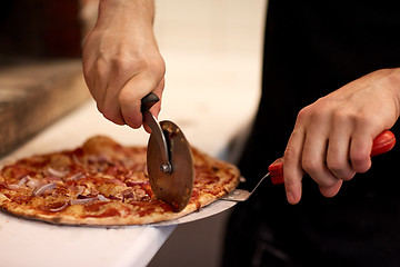 Image showing cook hands cutting pizza to pieces at pizzeria