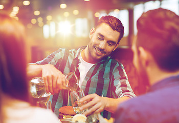 Image showing happy man with friends pouring water at restaurant