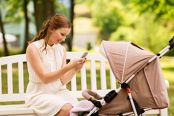 Image showing happy mother with smartphone and stroller at park