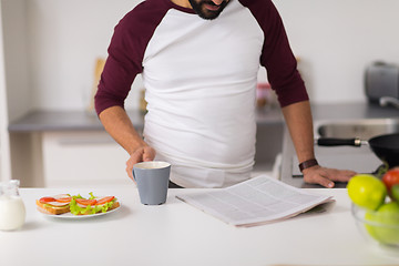 Image showing man reading newspaper and eating at home kitchen