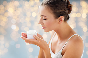 Image showing close up of happy woman holding and smelling cream