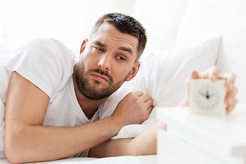 Image showing young man in bed reaching for alarm clock