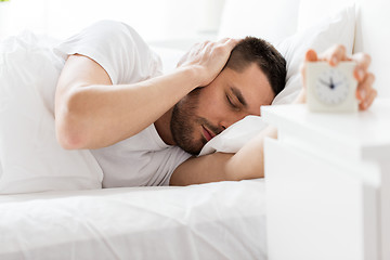 Image showing young man in bed reaching for alarm clock