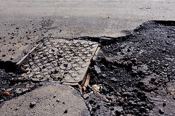 Image showing Damaged manhole cover on a road with broken tarmac