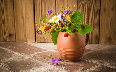 Image showing Ripe strawberries and a bouquet of forest flowers in a clay mug