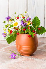 Image showing Ripe strawberries and a bouquet of forest flowers in a clay mug