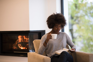 Image showing black woman reading book  in front of fireplace